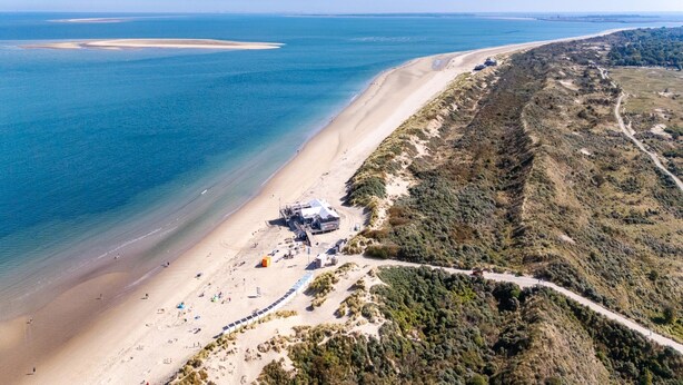 An aerial view of a beach with a sandy shore, a small building with a roof, and a road winding through the landscape. - Modern Chalet Near Beach in Renesse (Renesse)