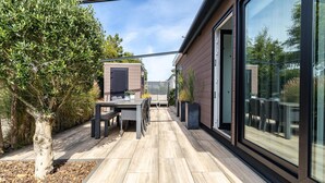 A modern outdoor patio with a wooden deck, a table with chairs, and a glass-enclosed room. - Modern Chalet Near Beach in Renesse (Renesse)