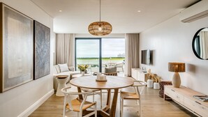 Un salon moderne avec une table ronde en bois, des chaises blanches, une grande fenêtre offrant une vue dégagée, un luminaire au plafond et un téléviseur fixé au mur.