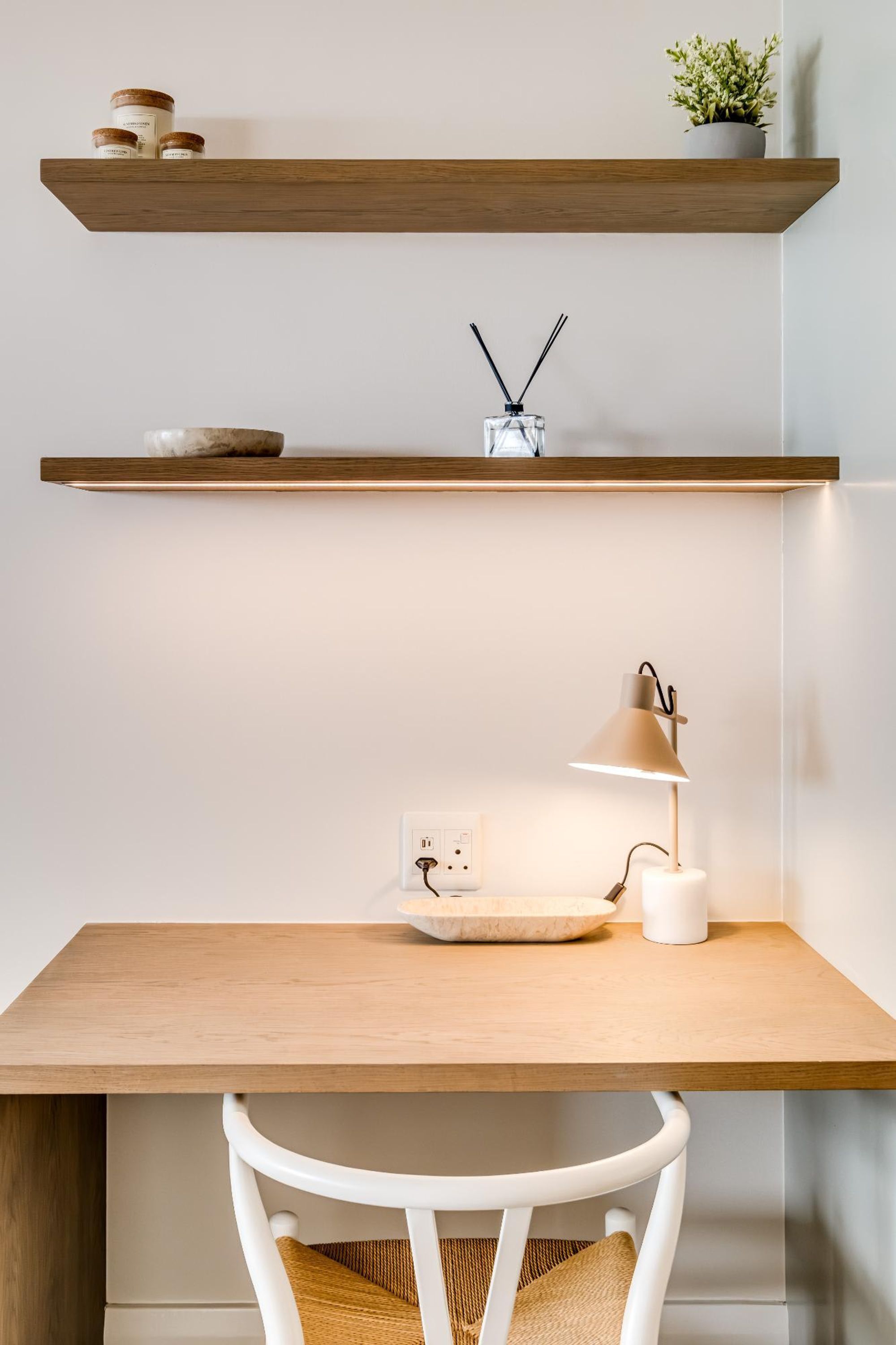 A workspace with a wooden desk, white chair, and two wooden shelves above.