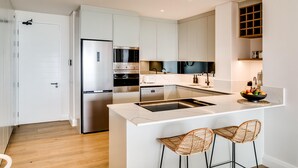 Une cuisine moderne avec des meubles blancs, un réfrigérateur en acier inoxydable, un îlot central doté de tabourets et un four encastré.