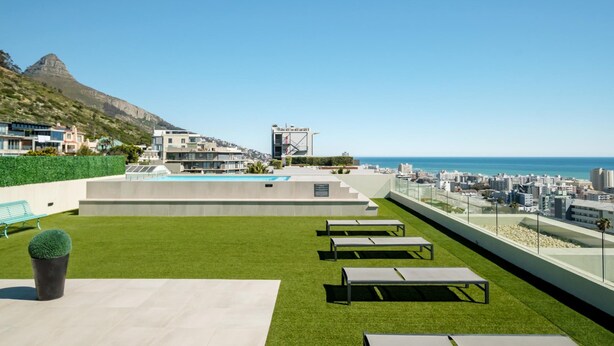 A rooftop terrace with artificial grass, seating areas, and a view of the ocean and cityscape. - Ocean View 1bed Apartment in Sea Point Marlo Cove (Cape Town)