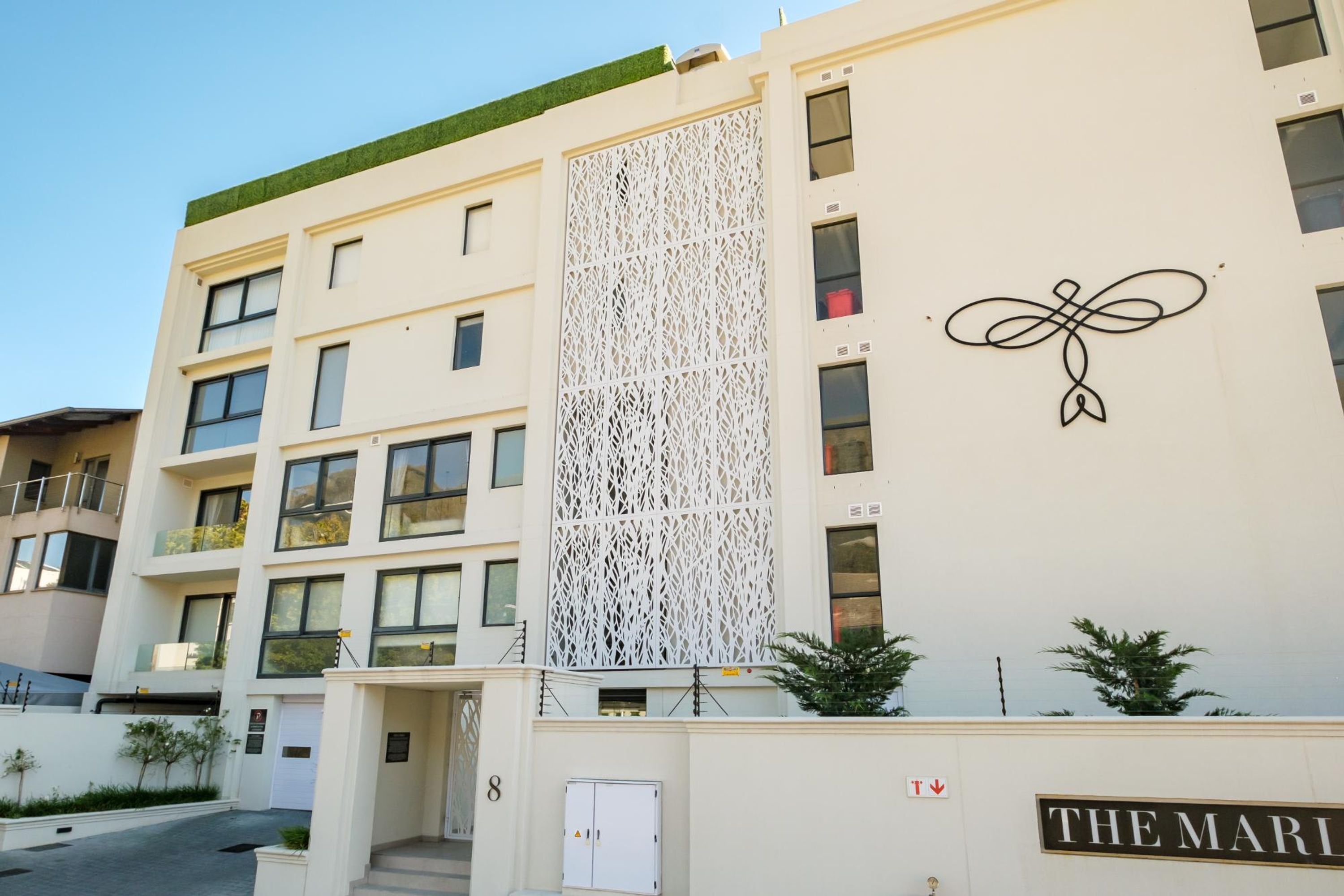 A multi-story building with a white facade, a decorative lattice panel, and a sign that reads "THE MARI".