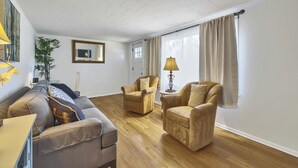 Un salon avec un canapé, deux fauteuils, une lampe et un miroir au mur.