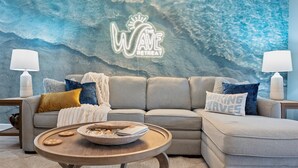 A living room with a grey sofa, a round wooden coffee table, and a neon sign reading "The Wave Retreat". - 2 Pools + 2 Hot Tubs + Sauna | Gated Beach Resort Condo (St. Augustine)
