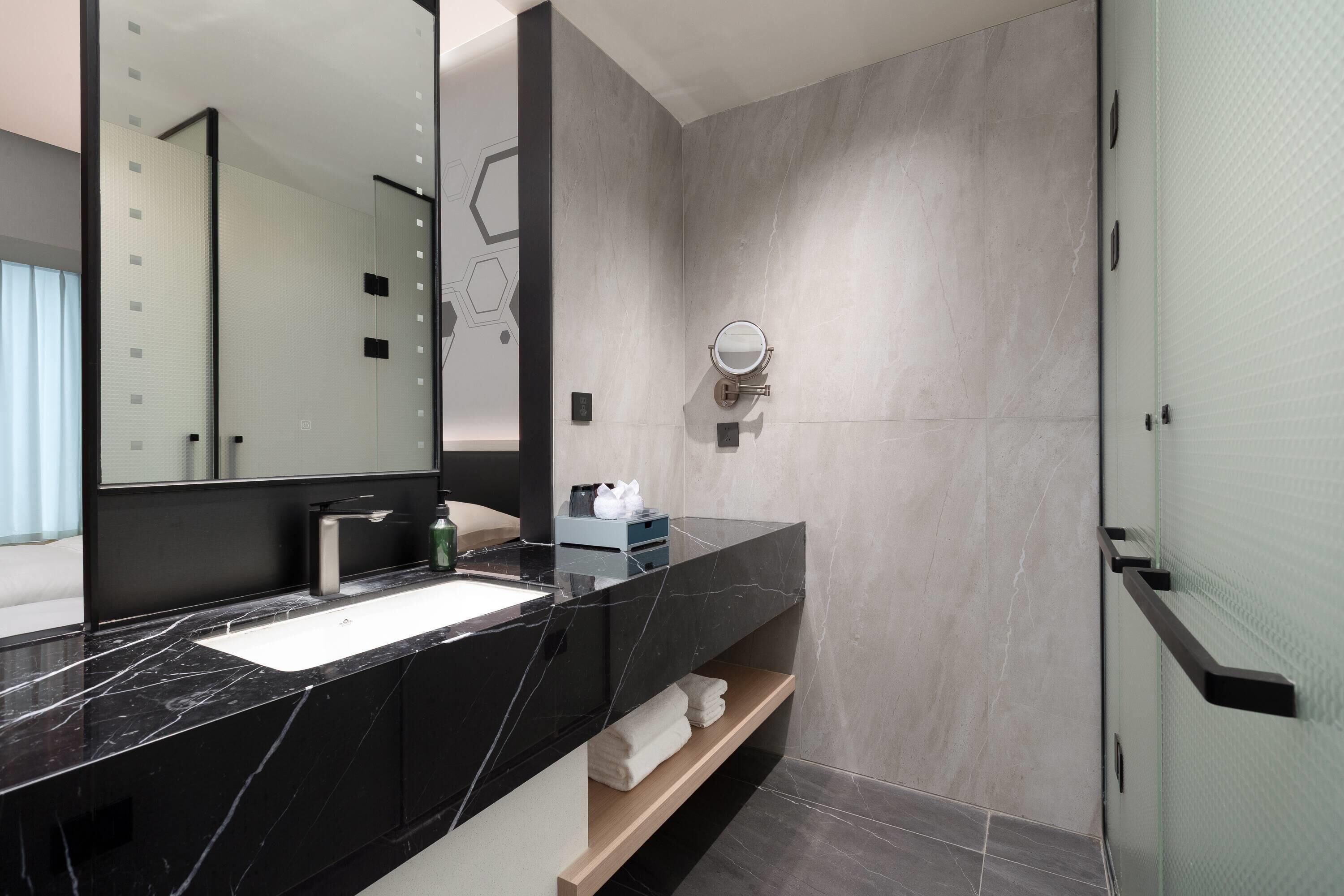 A modern bathroom with a black marble sink, a large mirror, and a glass shower enclosure.