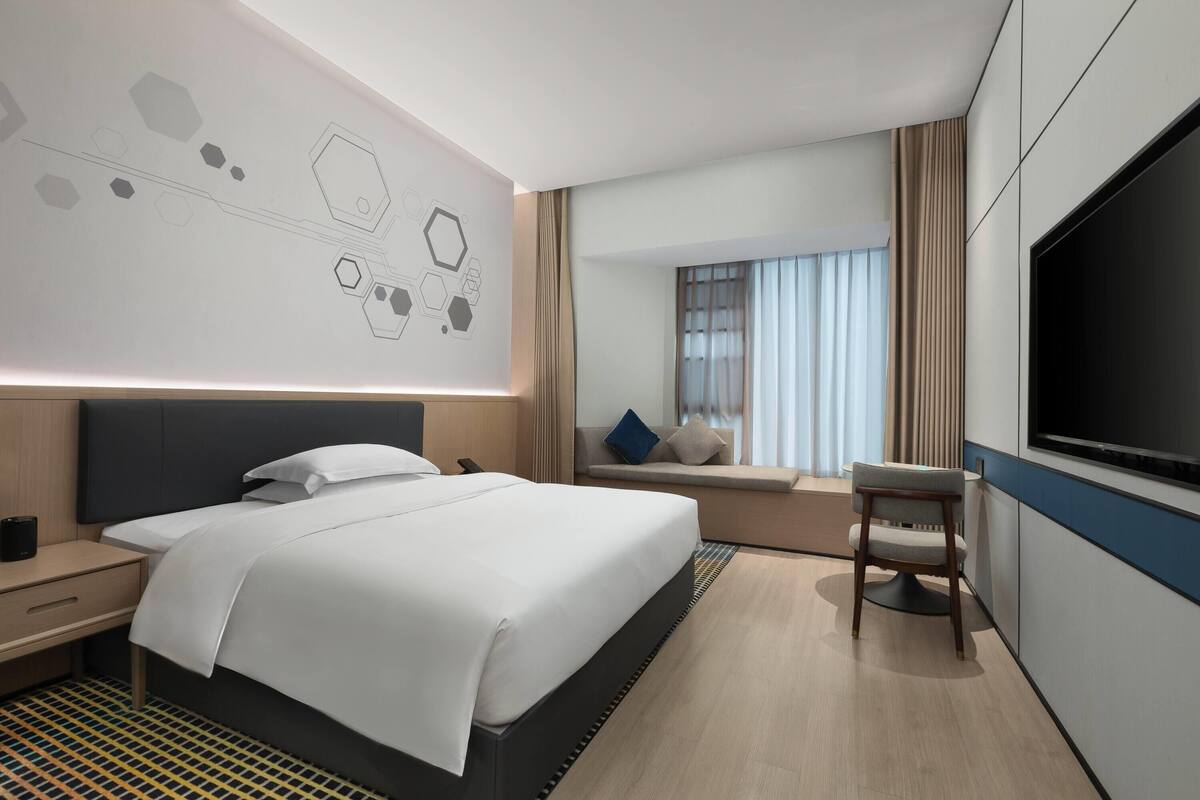 Une chambre d’hôtel moderne dotée d’un grand lit, d’une télévision, d’un coin salon avec vue et d’un sol à motifs.