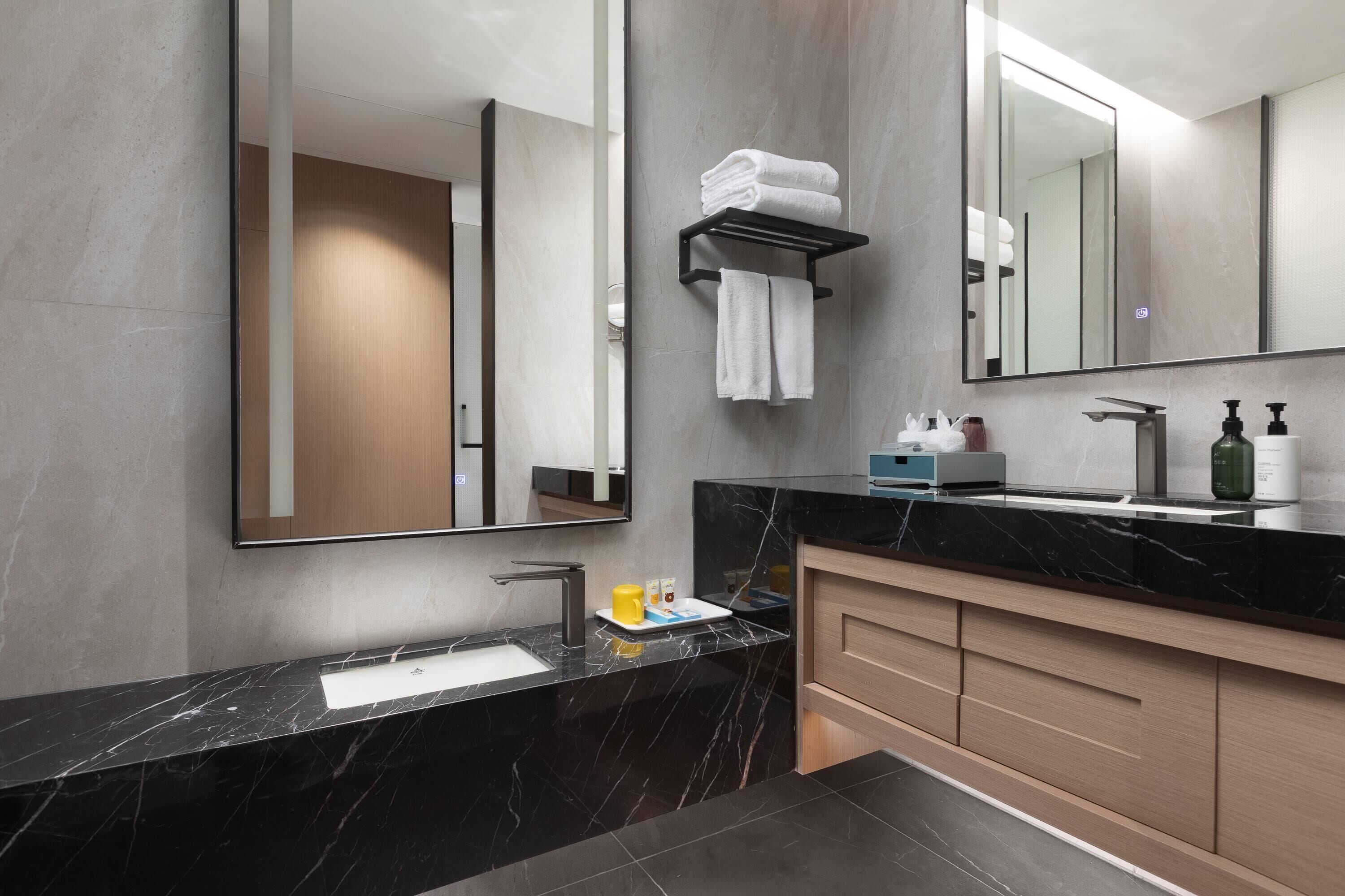 Un baño moderno con lavamanos de mármol negro, un espejo grande y un perchero para toallas.