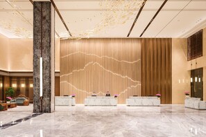 A hotel lobby with marble flooring, a reception desk, and a decorative wall.