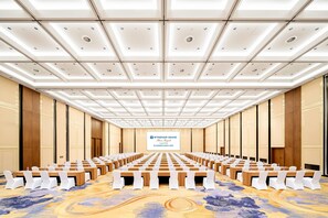 Une salle de conférence avec des rangées de tables et de chaises, un grand écran à l’avant et un tapis à motifs.