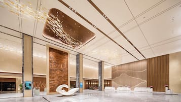 A spacious lobby with a large white sculpture, a reception desk, and a high ceiling with decorative lighting.
