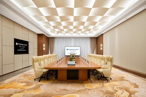 A conference room with a long table, multiple chairs, a projector screen, and a patterned carpet.