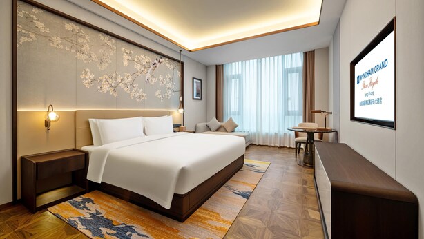 Habitación de hotel con una cama grande, mesitas de noche, un escritorio con silla, televisor y un ventanal con cortinas.