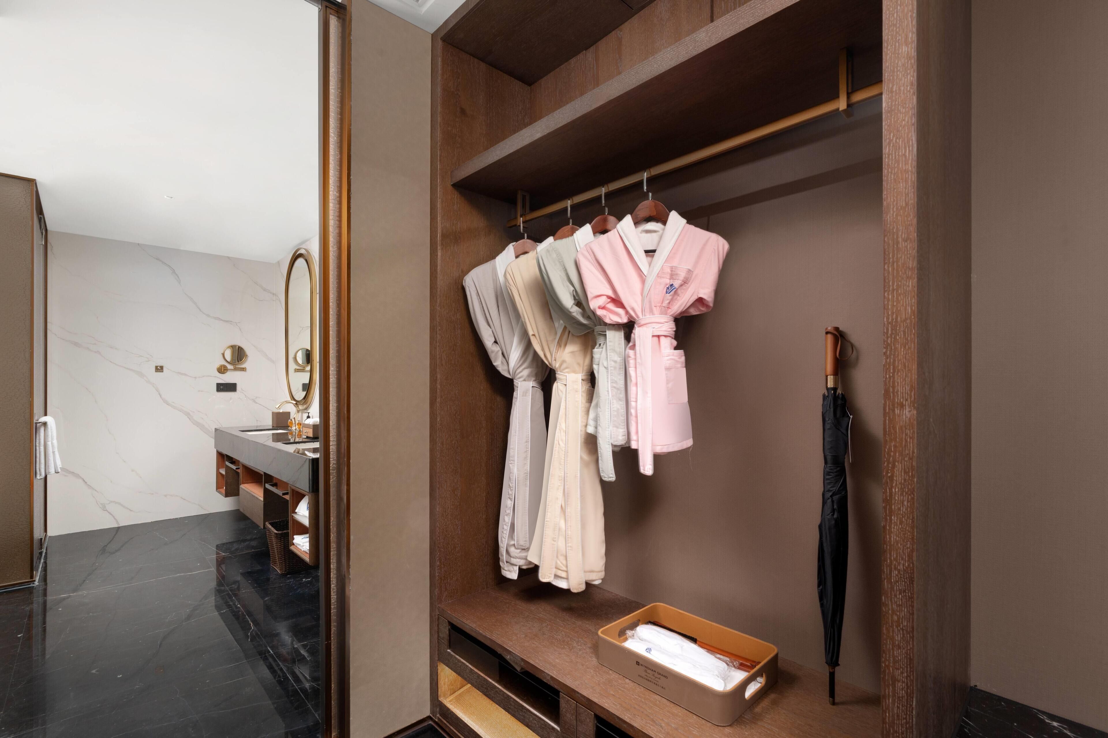 A modern bathroom with a marble floor, a wooden vanity, a mirror, and a robe rack with several robes.