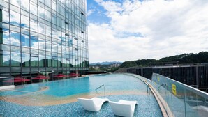 A modern hotel pool with a glass facade, lounge chairs, and a clear view of the surrounding landscape.