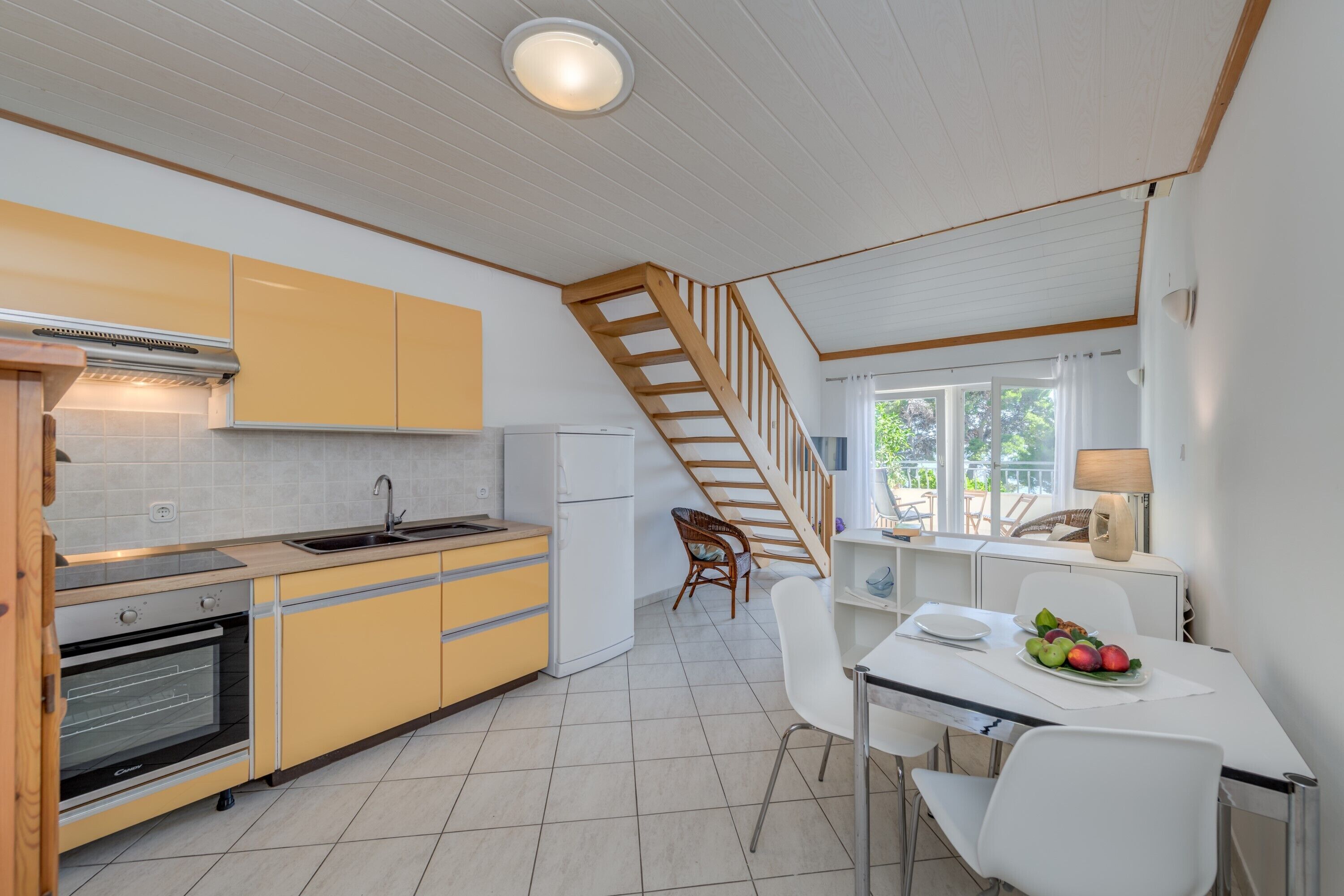 A modern kitchen with yellow cabinets, a wooden staircase, and a dining area with a table and chairs.