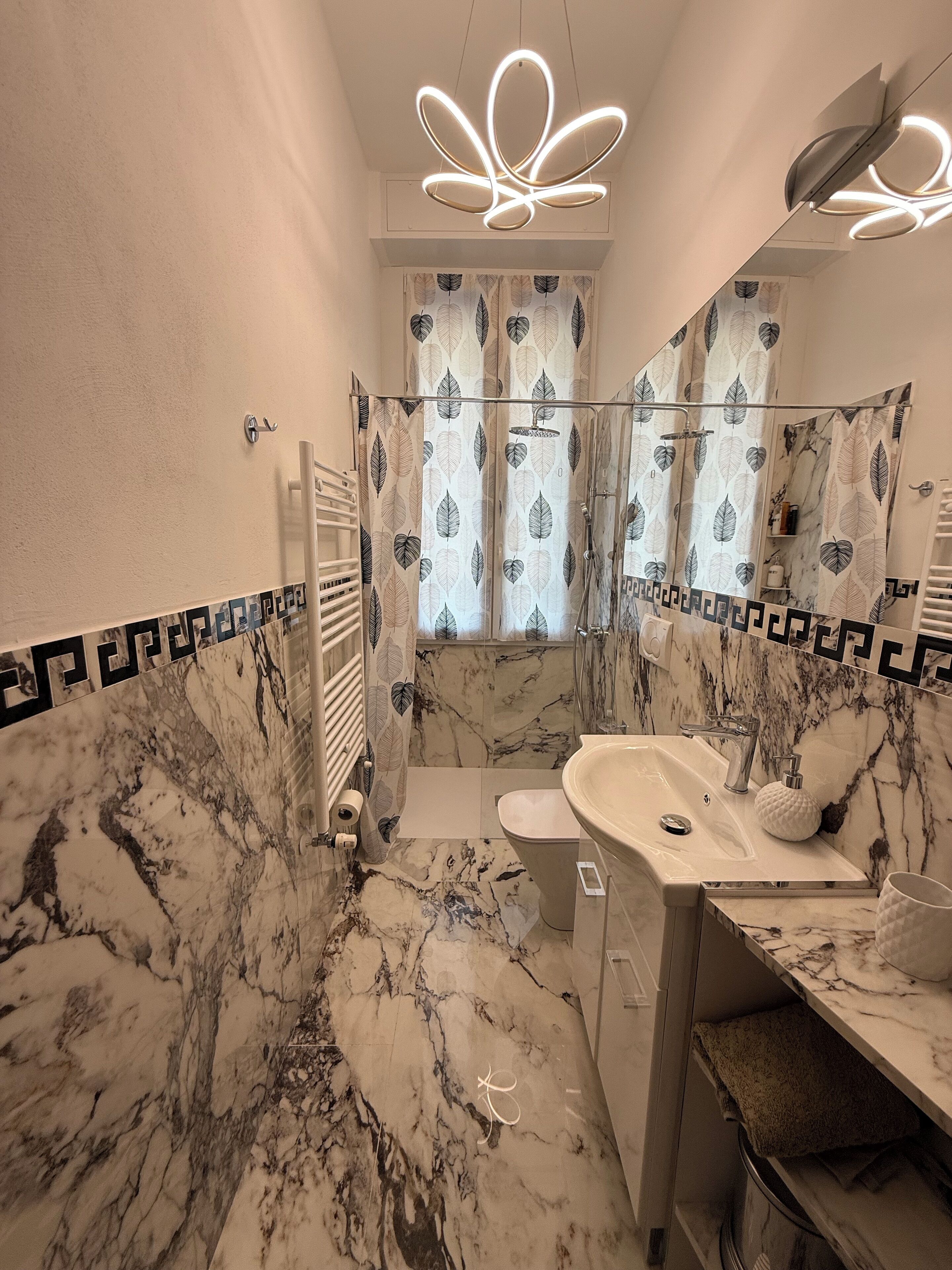 Ein modernes Badezimmer mit Marmorboden, einem Waschbecken mit Marmorplatte, einer Dusche mit einem blattmuster Vorhang und einer Deckenleuchte.