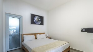 A bedroom with a bed, a door leading to a balcony, a framed picture on the wall, and a small bedside table with a lamp. - Laguna Park Apartments (Sosúa)