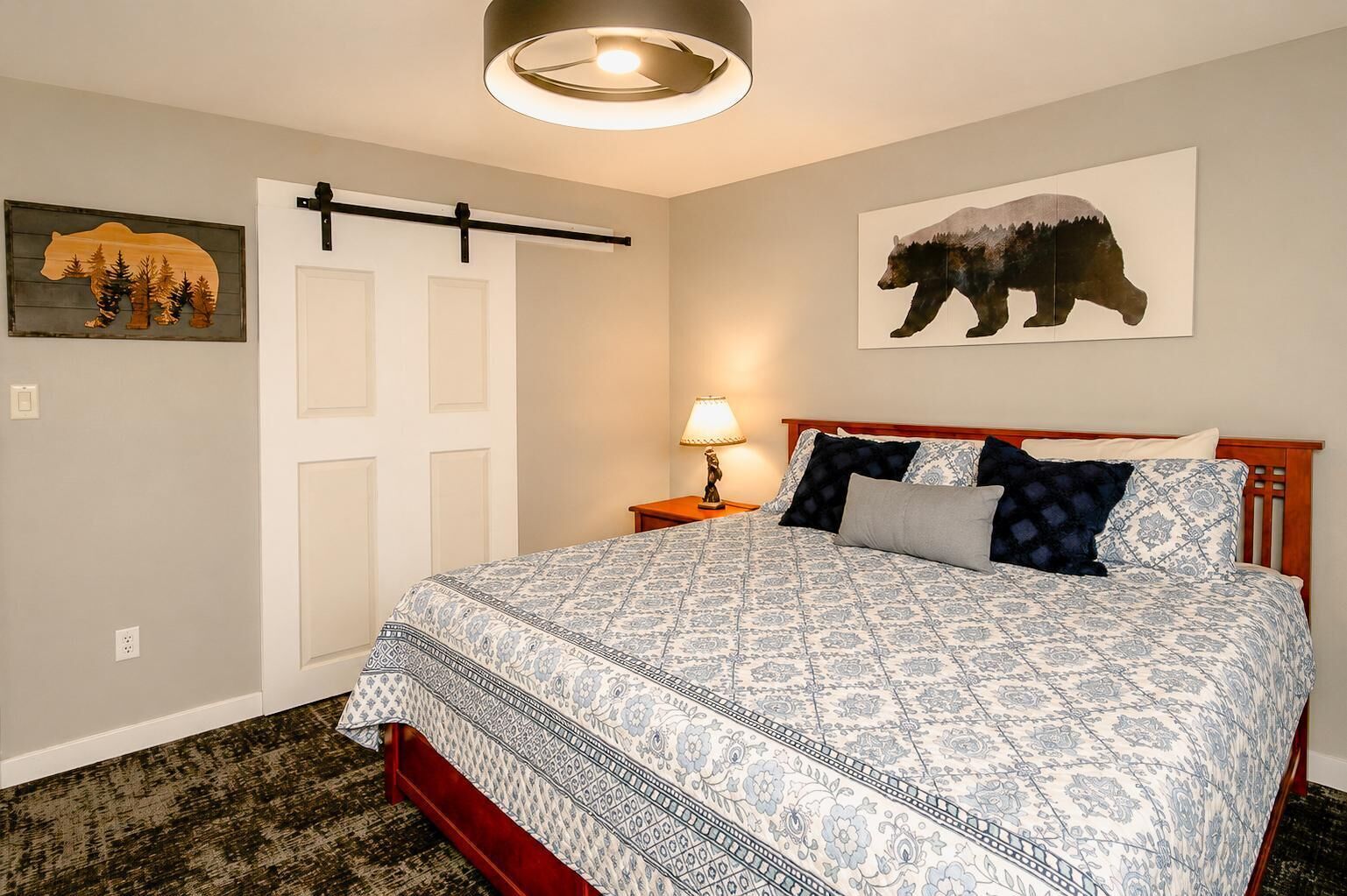 Een slaapkamer met een bed, een nachtkastje, een muurlamp, een deur en twee kunstwerken met berenmotieven.