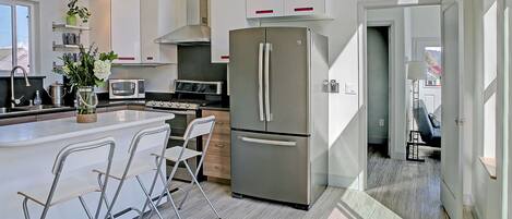 A modern kitchen with a central island, stainless steel appliances, and a view to the outside.