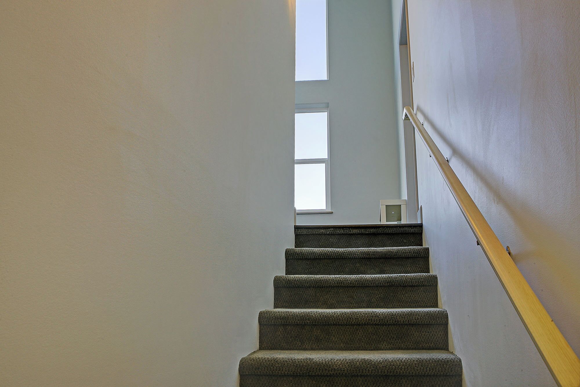 Una escalera con peldaños alfombrados y barandilla de madera, que conduce a un rellano con ventana.