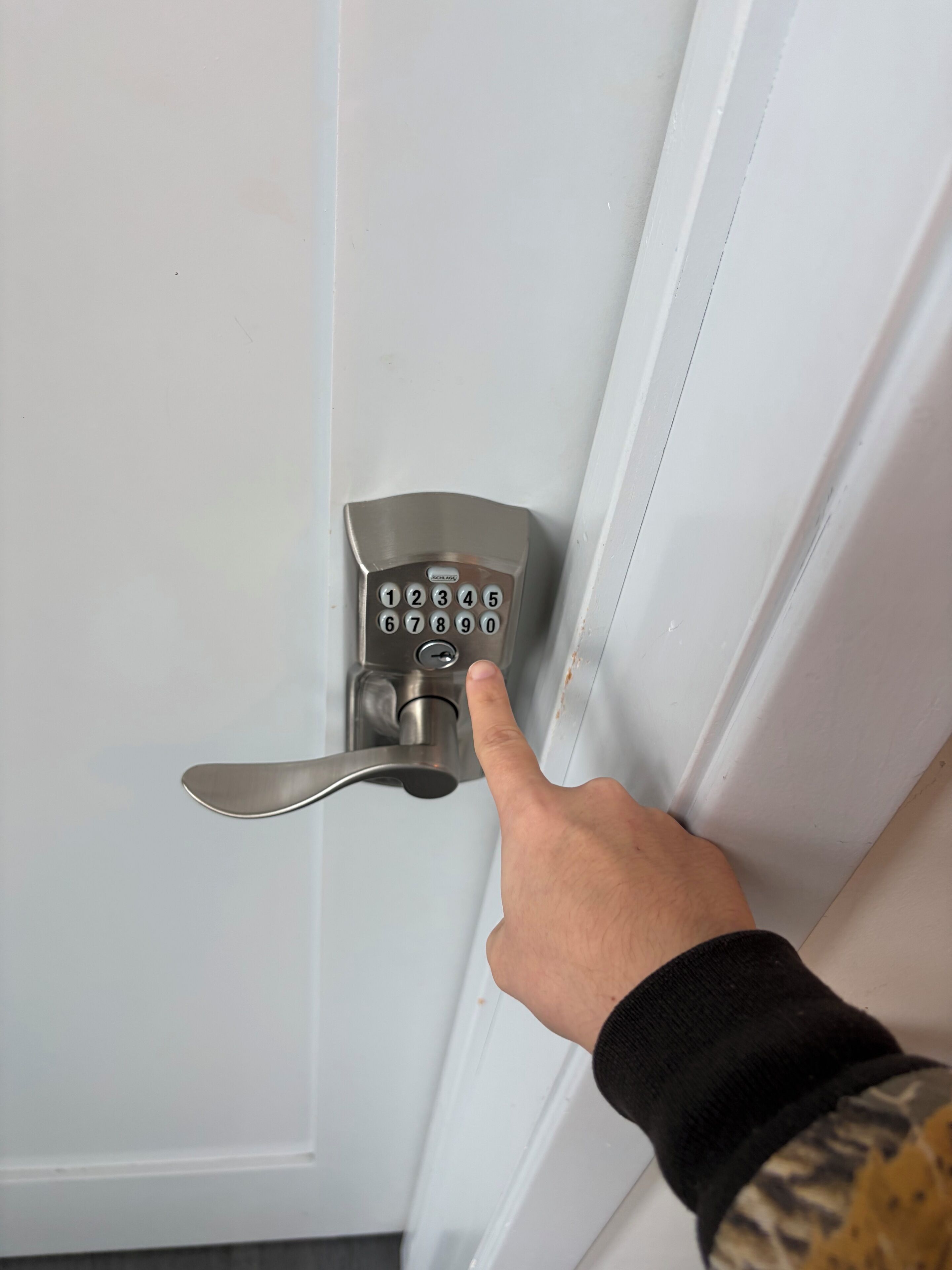 A hand pressing a numeric keypad on a door lock.