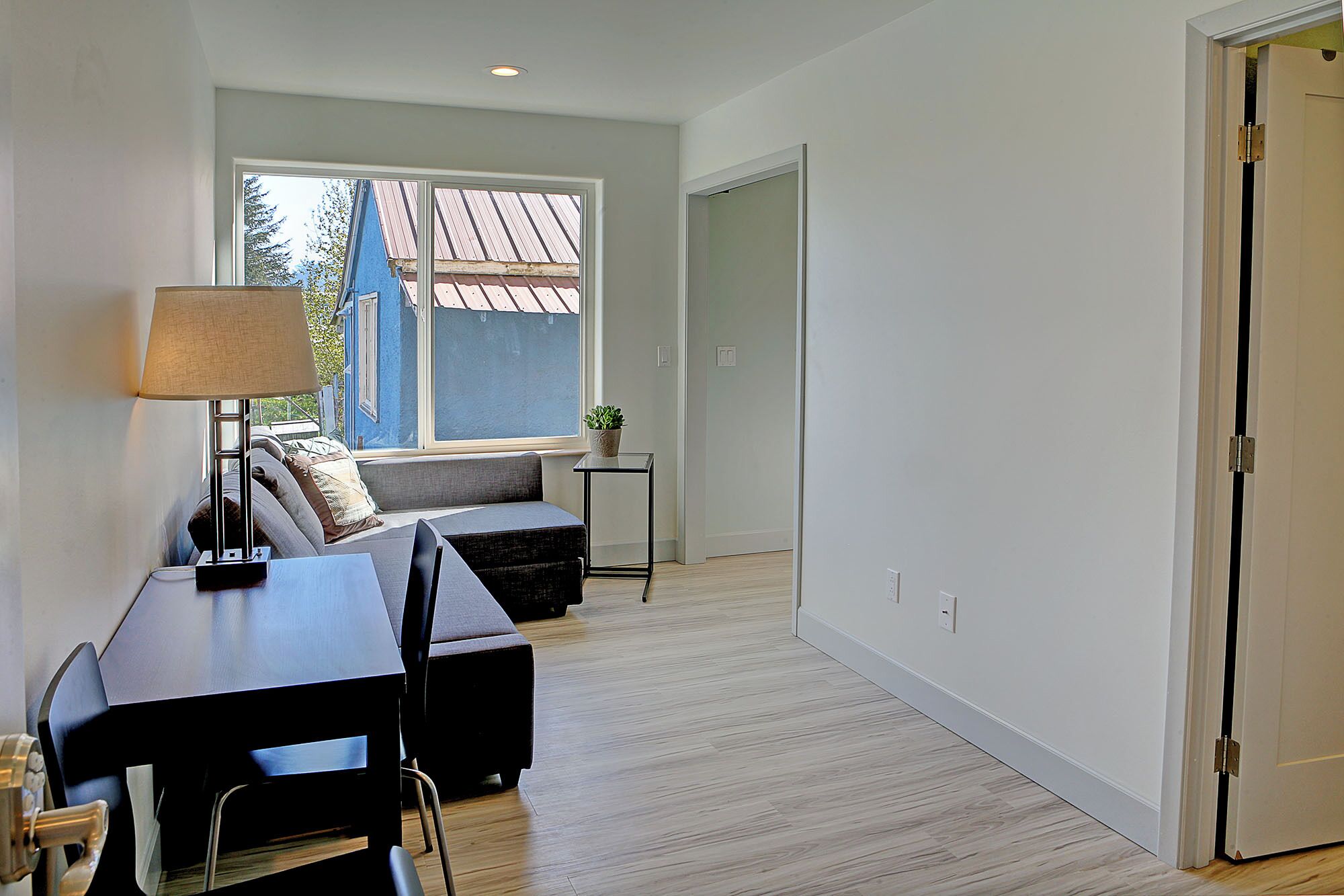 Un salon moderne avec un canapé, une table et une lampe. Une fenêtre offre une vue sur un bâtiment à l’extérieur.