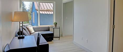 Un salon moderne avec un canapé, une table et une lampe. Une fenêtre offre une vue sur un bâtiment à l’extérieur.