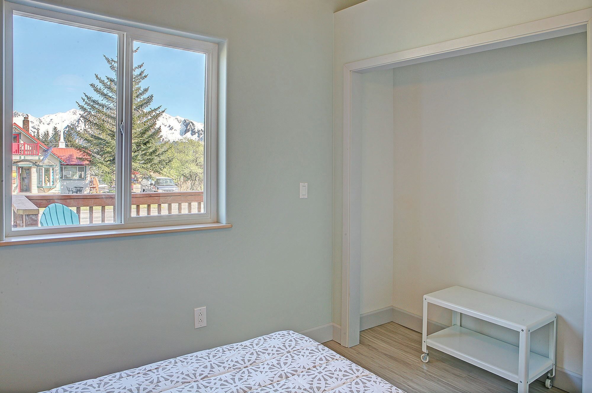 Ein Zimmer mit einem Bett, einem kleinen weißen Tisch, einem Fenster mit Blick auf Berge und ein Gebäude sowie einem Schrank.