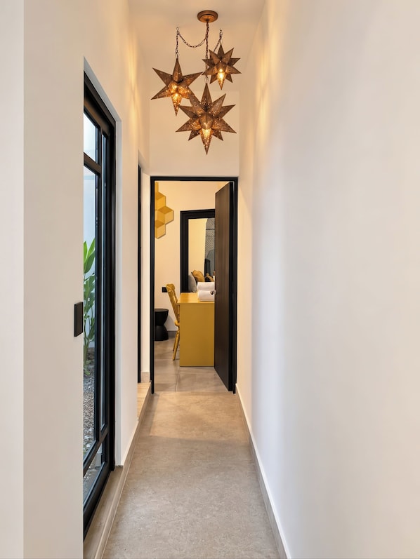A modern hallway with star-shaped hanging lights, a yellow bench, and a view into a room with a sink and towel.