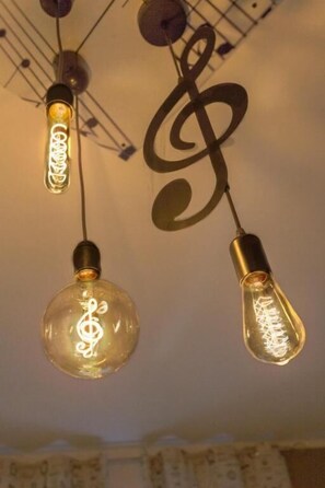 Two light bulbs with a treble clef design inside, hanging from a ceiling with a crisscross pattern. - segui le note della tua vita (Cremona)