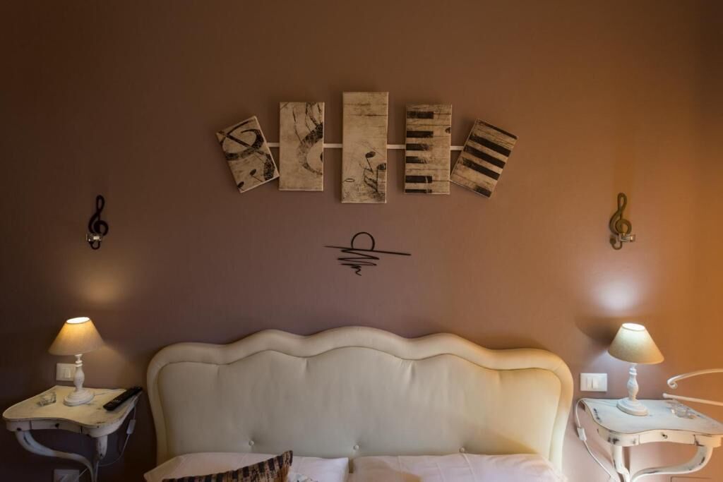 Une chambre à coucher avec une tête de lit blanche recouverte de tissu, deux tables de chevet avec des lampes et une œuvre d’art accrochée au mur au-dessus du lit.