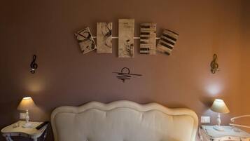 Une chambre à coucher avec une tête de lit blanche recouverte de tissu, deux tables de chevet avec des lampes et une œuvre d’art accrochée au mur au-dessus du lit.