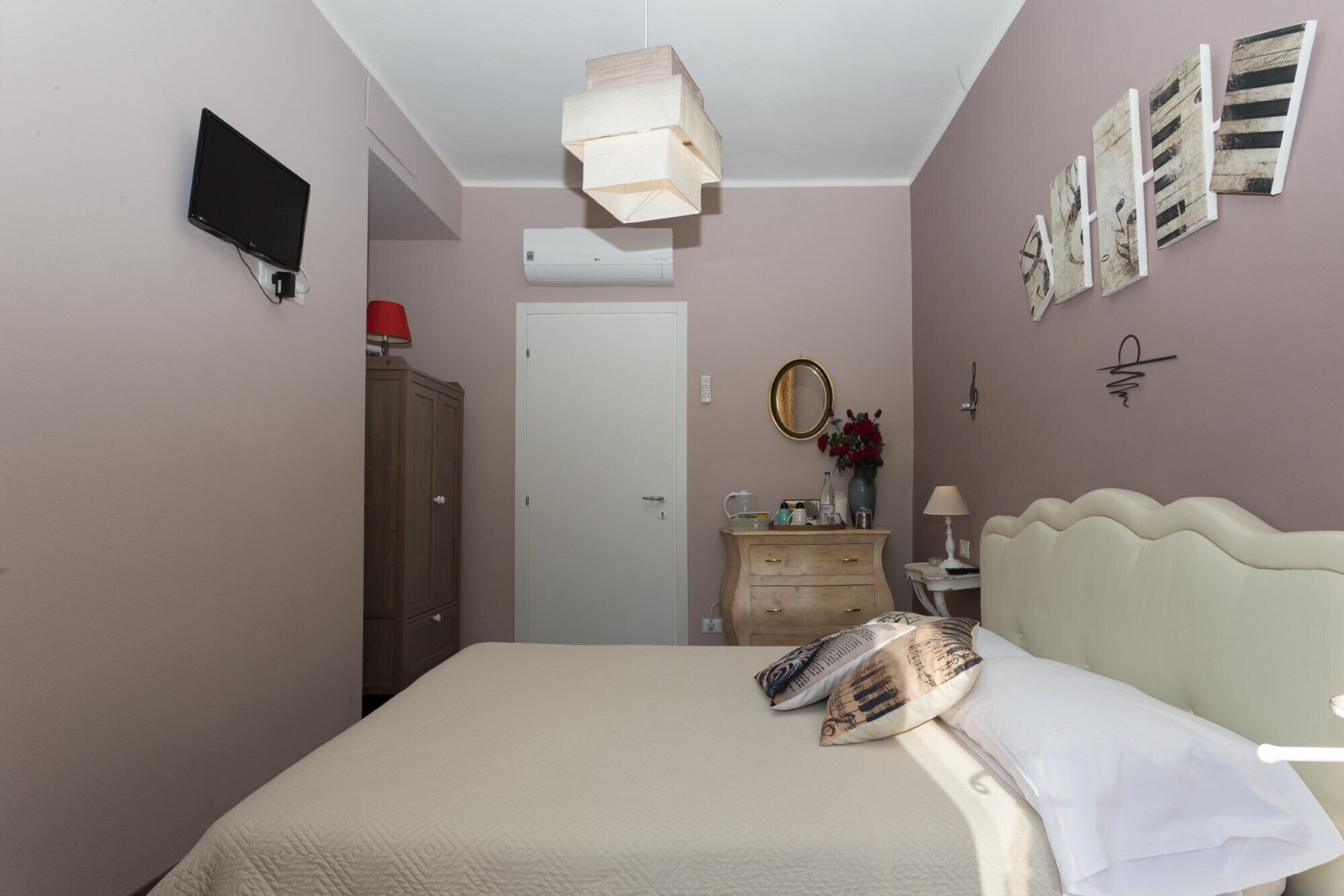 A bedroom with a bed, a dresser, a mirror, and a TV on the wall.