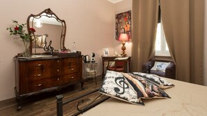 A bedroom with a wooden dresser, a mirror, a desk with a lamp, a chair, and a bed with decorative pillows.