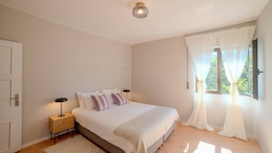 A bedroom with a bed, bedside tables, a nightstand, a window with curtains, and a ceiling light. - VIVA Spacious 3 bedroom apartment (Porto)