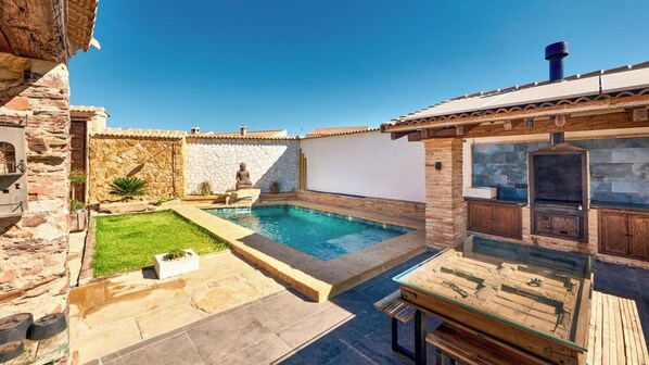 A backyard with a swimming pool, stone walls, and a wooden deck.