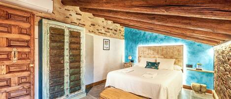 A bedroom with a wooden ceiling, a bed with white bedding, a wooden chest, and a blue accent wall.