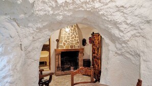 Un intérieur rustique avec une cheminée en pierre, des meubles en bois et un mur blanc à la texture particulière.