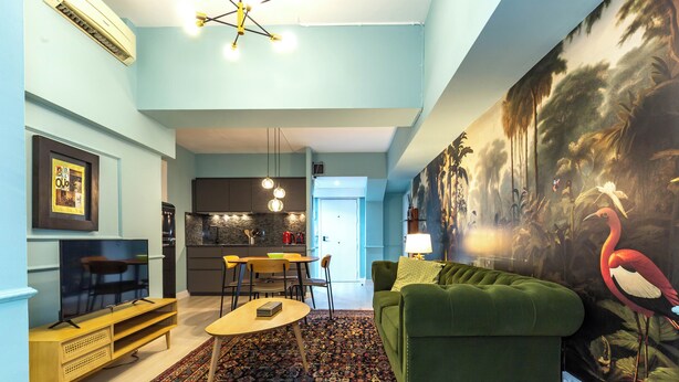 Een woonkamer met een groene bank, een salontafel en een televisie. Achtergrond is een keuken met een eethoek.