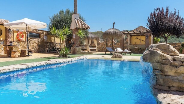 A swimming pool with a stone edge, surrounded by lounge chairs and a stone wall.