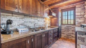 A rustic kitchen with wooden cabinets, a stone backsplash, and a large window providing natural light.