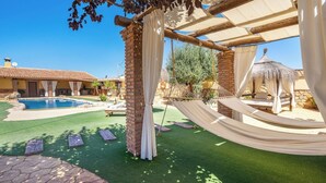 A pool area with a hammock and a thatched-roof structure.