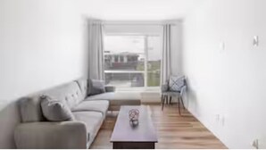 A modern living room with a sofa, a coffee table, and a view through large windows.