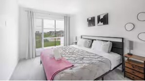 A modern bedroom with a bed, a bedside table, a window with curtains, and a view of the outdoors.