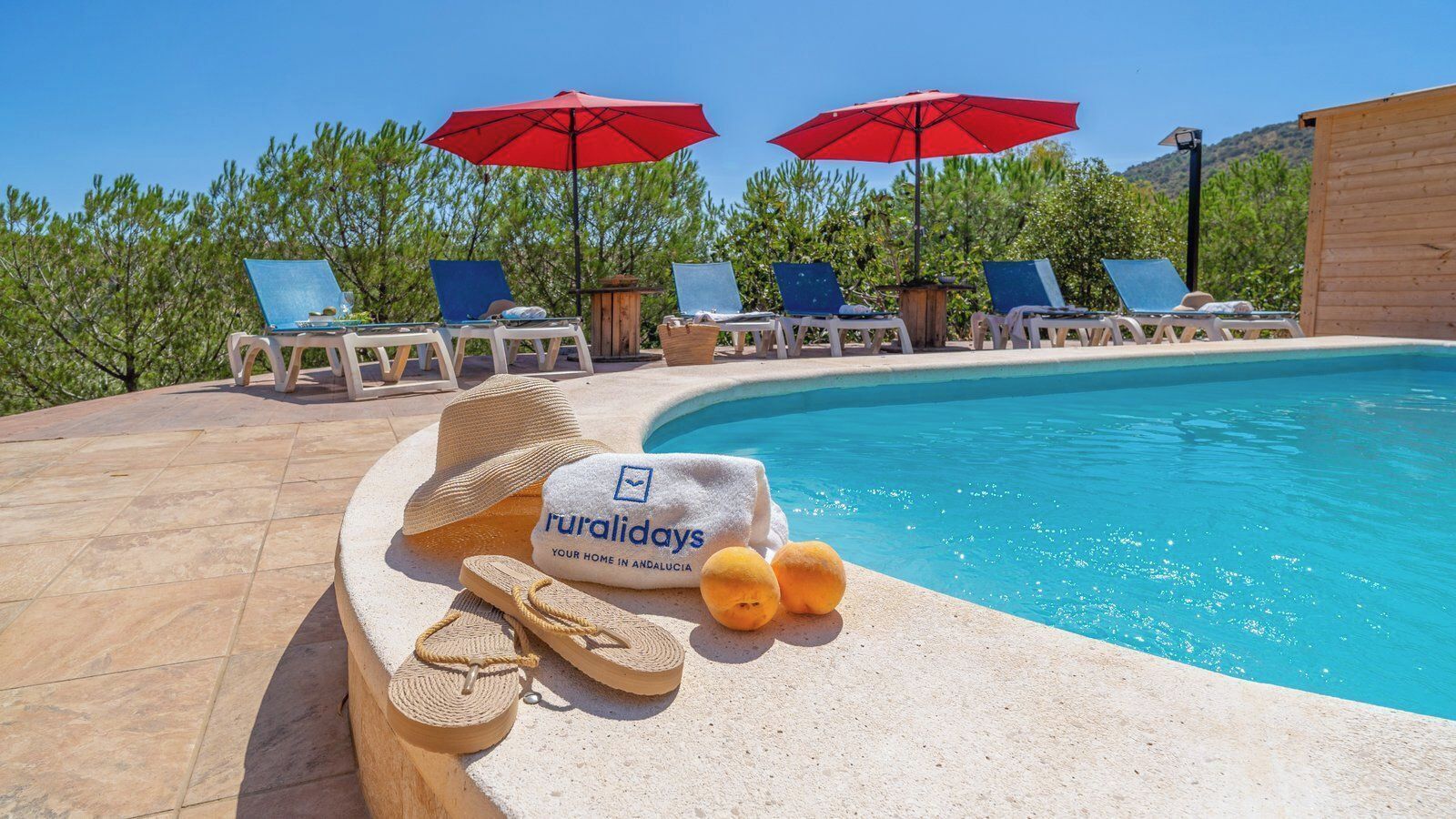 A poolside area with lounge chairs, umbrellas, and a sign for 'ruralidays'.