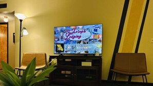 Ein Wohnzimmer mit Fernseher, der eine Willkommensnachricht zeigt, zwei Sessel, einer Lampe und einem Blumentopf.