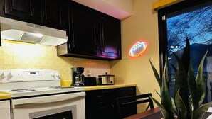 Eine Küche mit Herd, Kaffeemaschine und einem Neon-Schild an der Wand.