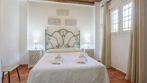 A neatly made bed with a decorative headboard, two bedside tables with lamps, and a window with curtains. - La Era del Bonete Constantina by Ruralidays (Sevilla)