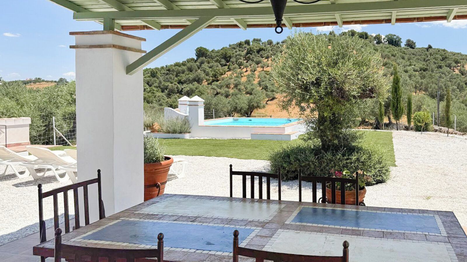 A covered outdoor seating area with a pool in the background.